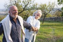 Senioren spazieren in ländlicher Umgebung, halten Händchen, albern herum — Stockfoto