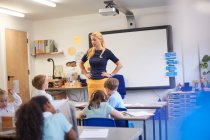 Lehrerin mit Hüftschwung vor Klasse in der Grundschule — Stockfoto