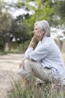 Mujer mayor sentada en un entorno rural, expresión reflexiva - foto de stock