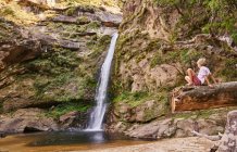Мальчик, сидящий на бревне, глядя на водопад, Самайпата, Санта-Крус, Боливия, Южная Америка — стоковое фото