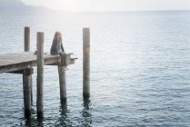Frau sitzt auf Holzsteg und schaut weg — Stockfoto