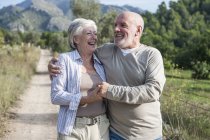 Старша пара йде разом у сільській місцевості, тримаючись за руки, посміхаючись — стокове фото