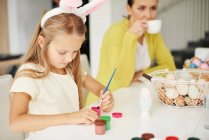 Девушка рисует крутое пасхальное яйцо за столом — стоковое фото