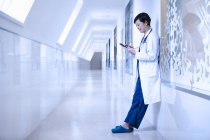 Лікар в лікарняному коридорі спирається на стіну за допомогою смартфона — стокове фото