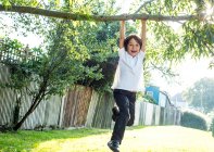 Мальчик веселится, качаясь на ветке дерева — стоковое фото