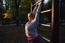 Curvaceous young woman gripping exercise bar in park — Stock Photo