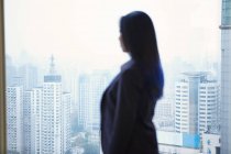 Вид сбоку на деловую женщину, смотрящую в окно на городской пейзаж — стоковое фото