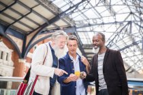 Drei reife Männer am Bahnhof, die aufs Smartphone schauen — Stockfoto