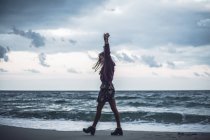 Молодая женщина идет по пляжу с поднятыми руками — стоковое фото