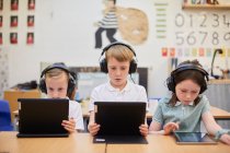 Schoolboy and girls listening to headphones in class at primary school — Stock Photo