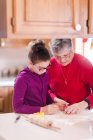 Girl and grandmother using cookie cutter on dough at kitchen counter — Stock Photo