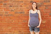Retrato de mujer adulta media embarazada por pared de ladrillo - foto de stock