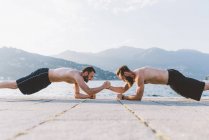 Two young men doing push ups on waterfront, Lake Como, Lombardy, Italy — Stock Photo