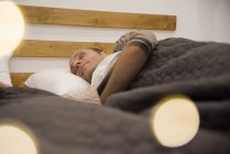 Mature man asleep under blanket in bed — Stock Photo
