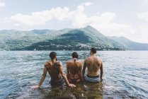 Vista trasera de tres amigos sentados en el lago Como, Como, Lombardía, Italia - foto de stock