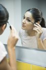 Woman applying mascara in front of mirror — Stock Photo