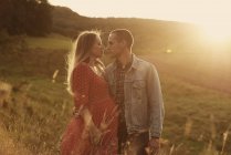Romantic pregnant couple standing face to face on hillside at sunset — Stock Photo