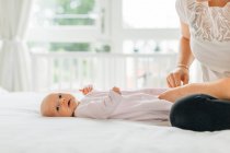 Junge Frau kleidet Baby-Tochter auf Bett — Stockfoto