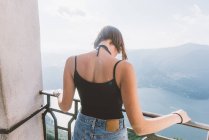 Vista trasera de la mujer joven en la plataforma de visualización mirando hacia abajo en el lago de Como, Lombardía, Italia - foto de stock