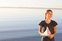 Young girl, standing near water, holding toy boat — Stock Photo