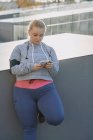 Изогнутая молодая женщина тренируется и смотрит на смартфон — стоковое фото
