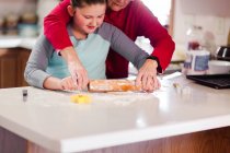 Дівчина і бабуся розкачують тісто печива разом на кухонній стійці — стокове фото