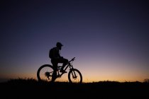 Силуэт горного велосипедиста, смотрящего на закат — стоковое фото