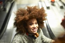 Молода жінка в навушниках посміхається на ескалаторі — стокове фото