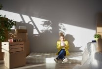 Jovem mulher sentada no colchão em nova casa e usando smartphone — Fotografia de Stock