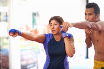 Mature woman practicing boxing punch with male trainer in gym — Stock Photo