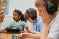 Escolares e meninas ouvindo fones de ouvido na sala de aula na escola primária — Fotografia de Stock