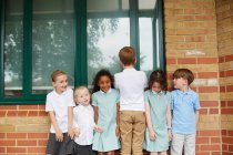 Estudantes e meninos de pé em uma fileira fora do prédio da escola primária, retrato — Fotografia de Stock
