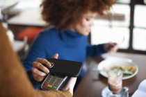 Client dans un café effectuant un paiement sans contact avec un téléphone mobile — Photo de stock