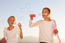 Дві молоді дівчата, на відкритому повітрі, дме бульбашки — стокове фото