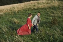 Pregnant couple strolling hand in hand in field — Stock Photo
