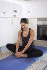 Молодая женщина делает упражнения на коврике на полу кухни — стоковое фото