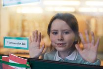 Portrait of schoolgirl with hands on classroom window at primary school — Stock Photo