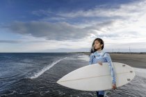 Joven surfista femenina mirando hacia la playa - foto de stock