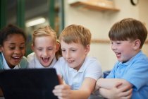 Школярі та дівчата сміються в цифровому планшеті в класі в початковій школі — стокове фото
