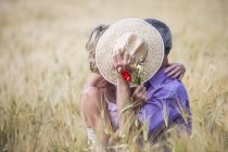 Couple in field in tall grass covering faces with straw hat — Stock Photo