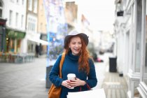 Молода жінка ходить вулицею, тримає чашку кави і сумку для покупок — стокове фото