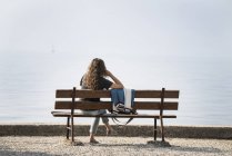 Вид сзади женщины, сидящей на скамейке и смотрящей на озеро — стоковое фото