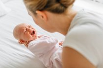 Jovem mulher embalando chorando bebê filha na cama — Fotografia de Stock