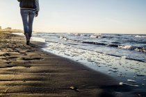 Blick auf eine barfüßige Frau, die am Ufer des Wassers am Strand von Riccione, Emilia-Romagna, Italien spaziert — Stockfoto