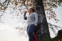 Курчавая молодая женщина тренируется и пьет бутилированную воду в парке — стоковое фото