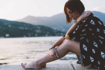 Jovem mulher sentada na parede à beira-mar pelo Lago de Como, Lombardia, Itália — Fotografia de Stock