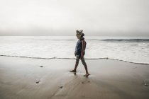 Niño de pie en la playa y mirando hacia otro lado - foto de stock
