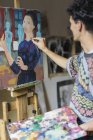 Artiste masculin peignant sur chevalet en atelier d'artiste — Photo de stock