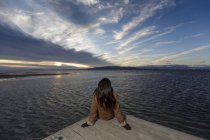 Молода жінка дивиться з пірсу на заході сонця — стокове фото