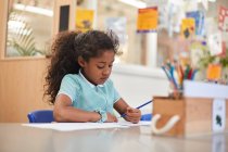 Школярка пише в класі на робочому столі в початковій школі — стокове фото